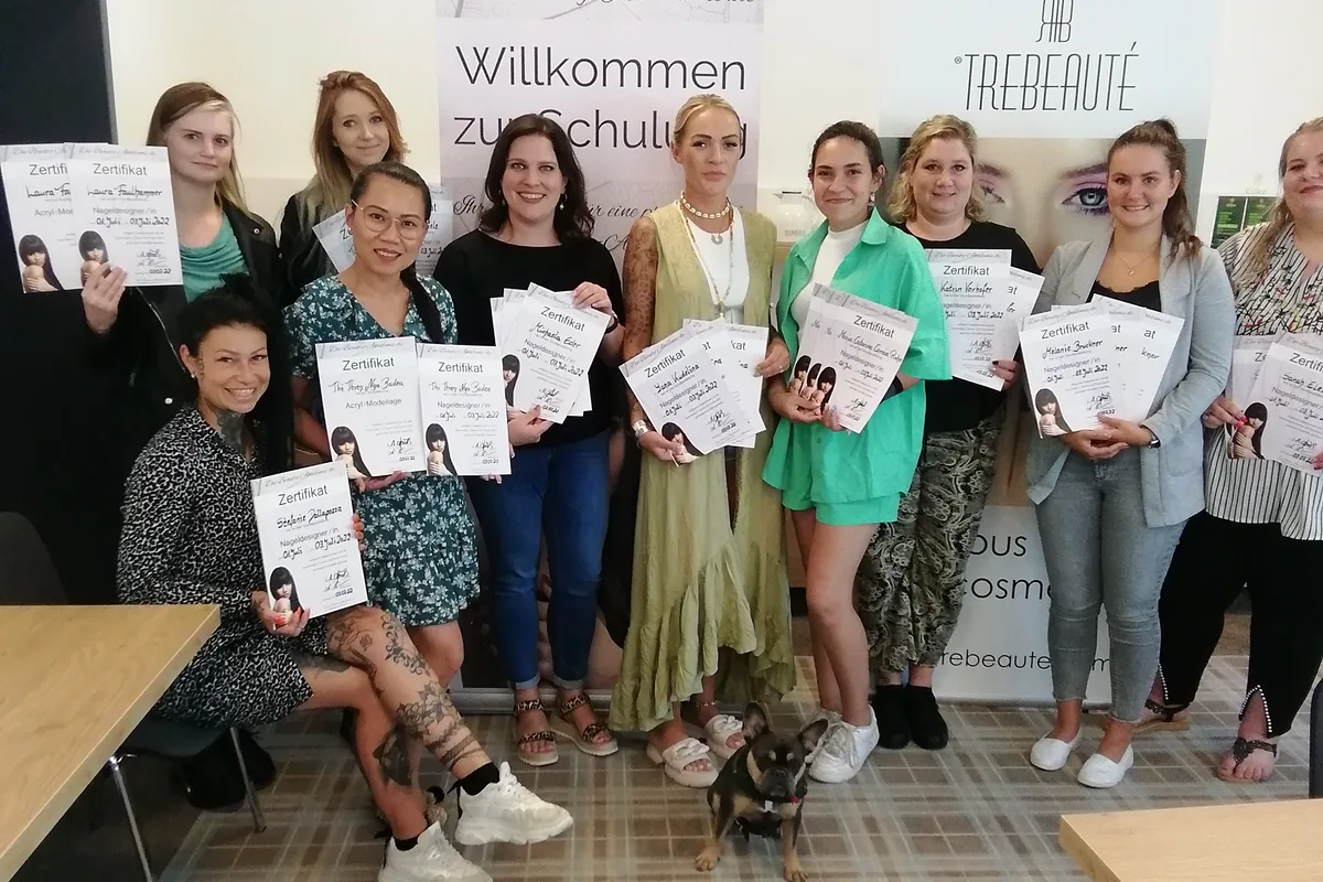 Absolventinnen einer Nageldesign-Ausbildung der Beauty Akademie stehen mit ihren Zertifikaten vor dem Rollup „Willkommen zur Schulung“.