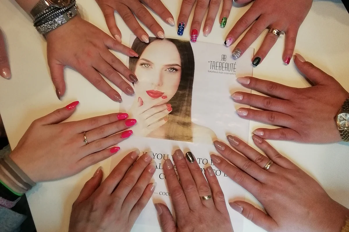 Hände mit fertigen Nagelmodellagen im Kreis auf einem Tisch: Gelnägel in Rosé, Pink und French sowie Nail-Art in Grün, Blau und Gold.